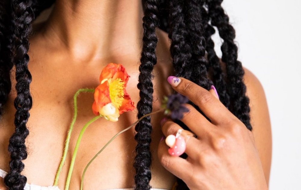 A hand with a mushroom ring holding orange poppies among long braids. Photograph by Hk.